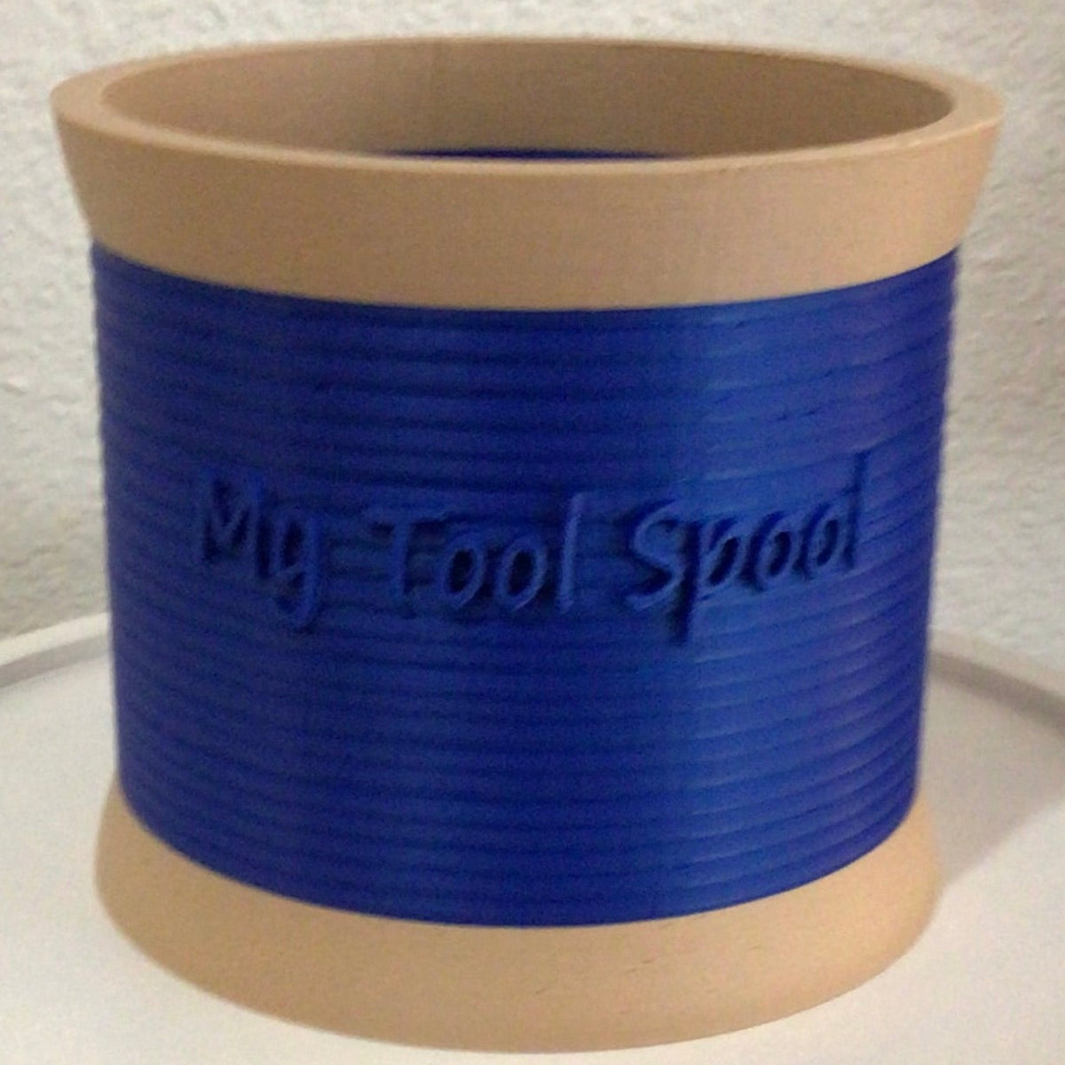 A 3-D printed craft or office supply organizer made in the image of a spool of thread with separate compartments with the words 'My Tool Spool' in 3D lettering.