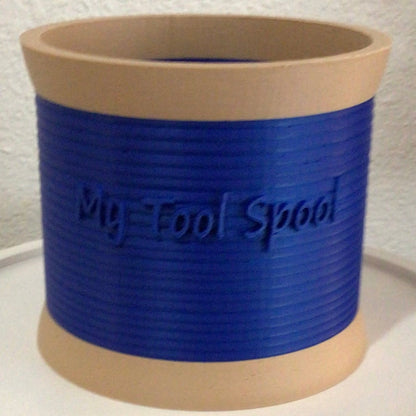 A 3-D printed craft or office supply organizer made in the image of a spool of thread with separate compartments with the words 'My Tool Spool' in 3D lettering.